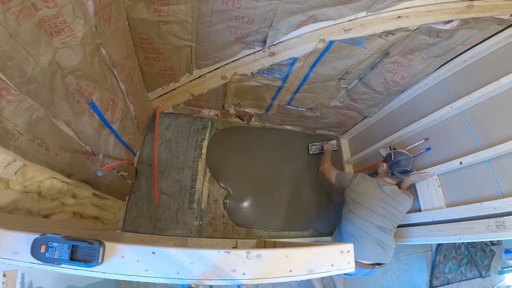 man spreading out self-leveling compound in unfinished shower space