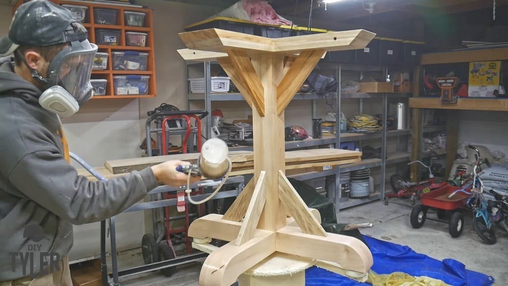 man applying spray finish to pedestal game table
