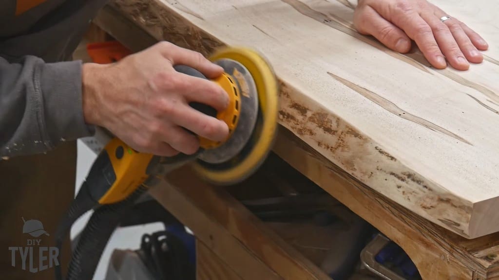 man sanding edge of slab tabletop for pedestal game table